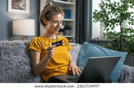Cheerful curly woman wears yellow shirt using laptop for purchase online, shopping from home concept Royalty-Free Stock Photo #2361734997