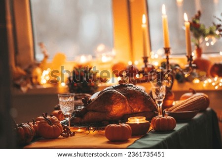 Thanksgiving day dinner with holiday autumn decor and candles. Family dining room table set with delicious golden roasted turkey on platter garnished rosemary fresh small pumpkins