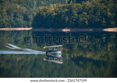A small boat glides across the smooth surface of lake. The shores with dense forest