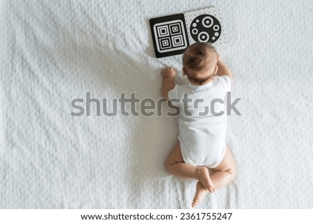 A baby looks at a black and white contrast educational book. Intellectual development of newborns. Developing cards for children. Royalty-Free Stock Photo #2361755247