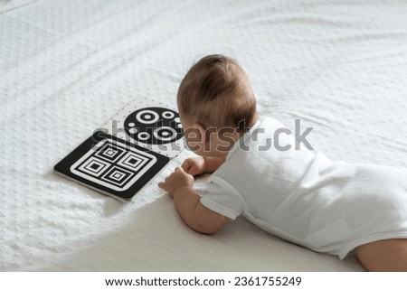 A baby looks at a black and white contrast educational book. Intellectual development of newborns. Developing cards for children. Royalty-Free Stock Photo #2361755249