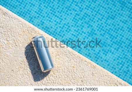 An aluminum can of beer lies by the pool. View from above.