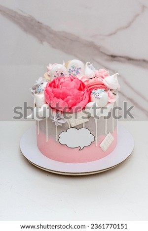 Beautiful and elegant grey and pink cake decorated with melted white chocolate, macaroons, edible peony flower and meringue kisses on marble background