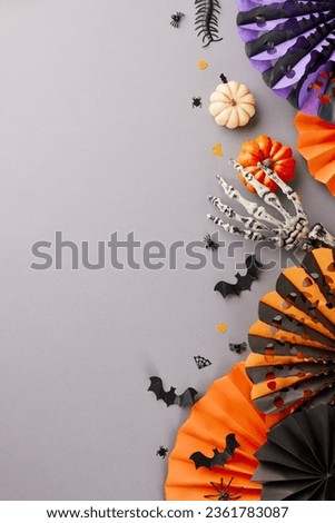 Revering the enigmatic allure of the Halloween season's arrival. Top view vertical photo of skeleton hand, paper party props, pumpkins, creepy insects on grey background with ad zone