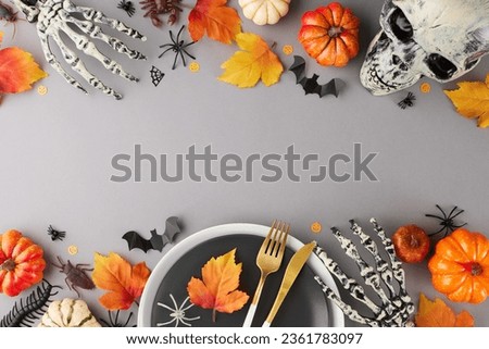 Infusing your table with the festive spirit of Halloween. Top view photo of plates, cutlery, skeleton hands, skull, colorful pumpkins, spooky insects, autumn leaves on grey background with promo zone