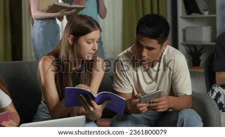 Medium shot of a boy and a girl sitting on a couch in a group of teens, young people, friends, studying, preparing for an exam, discussing, looking at their notes. Royalty-Free Stock Photo #2361800079
