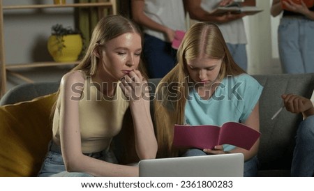 Medium shot of two girls sitting on a couch in a group of teens, young people, friends studying, preparing for an exam, discussing, looking at their notes. Royalty-Free Stock Photo #2361800283