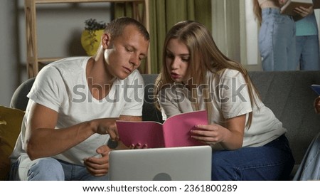 Medium shot of a boy and a girl sitting on a couch in a group of teens, young people, friends, studying, preparing for an exam, discussing, looking at their notes. Royalty-Free Stock Photo #2361800289