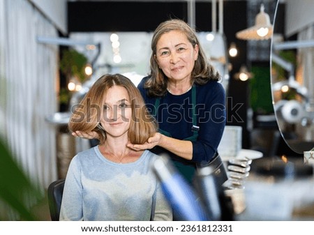 Elderly woman professional hair stylist discussing young female customer preferences in salon, choosing new hairdo . Royalty-Free Stock Photo #2361812331
