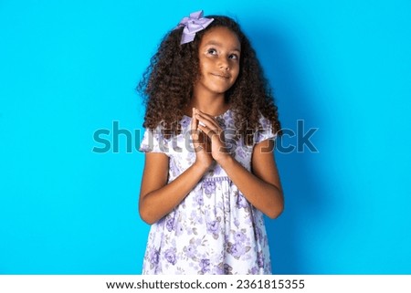 Charming cheerful beautiful kid girl with afro curly hairstyle wearing flowered dress making up plan in mind holding hands together, setting up an idea.