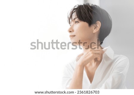 A profile portrait of an Asian woman. A Japanese woman is smiling by the window.She has short dark brown hair and wears a white shirt. Royalty-Free Stock Photo #2361826703