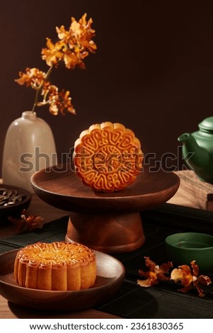Delicious Chinese traditional mooncakes displayed on wooden dishes. Green tea set arranged behind with a flower pot. A time of year that the moon is at its brightest