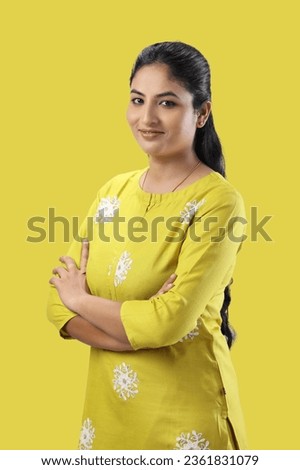 Beautiful Indian girl standing in confidence pose with folding hands yellow dress isolated on yellow background   Royalty-Free Stock Photo #2361831079