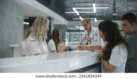 Family with little child stands near reception desk in hospital lobby. Woman fills out documents and papers, makes appointment with doctor. Medical staff work in modern medical center. Health care.
