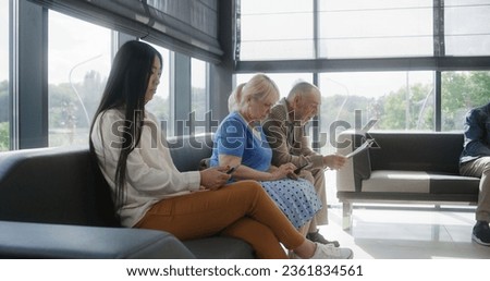 Diverse multicultural people sit on couches in clinic lobby area, wait for appointment with doctor or medical test results. Waiting area in medical center with modern design. Healthcare system. Royalty-Free Stock Photo #2361834561