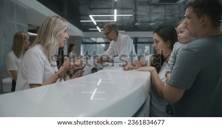 Family with little child stands near reception desk in clinic lobby area. Woman fills out documents and papers, makes appointment with doctor. Medical staff work in modern hospital. Health care. Royalty-Free Stock Photo #2361834677