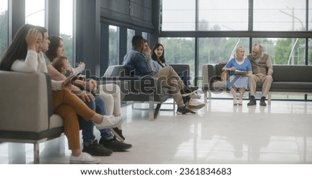 Diverse multiethnic people sit on couches in clinic lobby area, wait for appointment with doctor or medical test results. Waiting area in medical center with modern design. Healthcare system. Royalty-Free Stock Photo #2361834683
