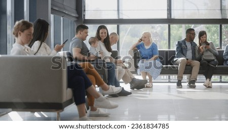 Diverse multicultural people sit on couches in clinic lobby area, wait for appointment with doctor or medical test results. Waiting area in medical center with modern design. Healthcare system. Royalty-Free Stock Photo #2361834785