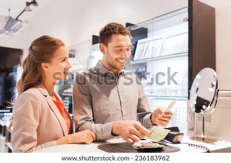 sale, consumerism, shopping and people concept - happy couple with money paying for purchase in jewelry store