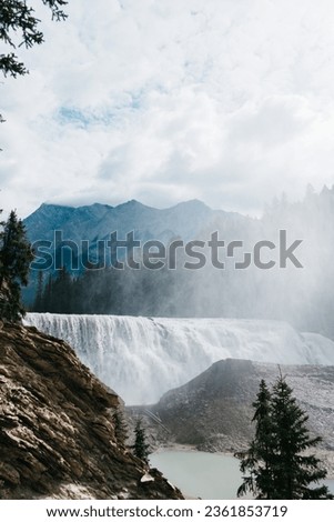 British Colombia waterfall with mountains in the background. The picture contains spray giving it a beautiful hazy look.