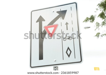 bike bicycle lane turn branch off bend yield rectangle traffic sign white black red with sky and tree branches behind
