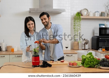 Young couple mixing fruit in a food processor, making a smoothie. Husband and wife having fun with smoothie in the kitchen and looking at each other. Healthy nutritious lunch snack smoothie.