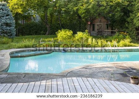 Backyard with outdoor inground residential swimming pool, garden, deck and stone patio Royalty-Free Stock Photo #236186239