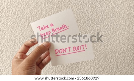 'Take a deep breath' and 'Don't quit!' words written on a white blank card, hold by a hand. Textured  background.