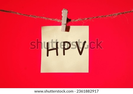 HPV Human papillomavirus text on a yellow sticker hanging on a rope with clothespins on a red background