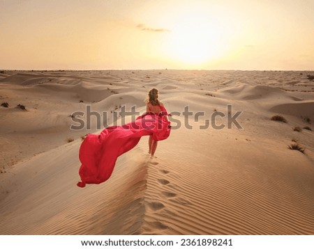Desert adventure. Young arabian Woman in red silk dress in sands dunes of UAE desert at sunset, fantastic view. The Dubai Desert Conservation Reserve, United Arab Emirates.