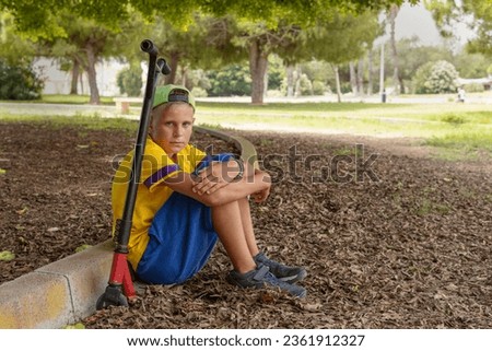 teenager in casual clothes sitting in the park on a scooter relaxing, active lifestyle of a child