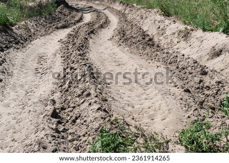 Sand road in the forest. Tire pattern of quad bike on driveway. Track imprint of quadricycle on nature land. Sand texture off road. Path in forest close up. Sand mounds and green forest in sunny day. Royalty-Free Stock Photo #2361914265