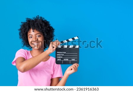 african american girl smiling in pink t-shirt with movie clapperboard in hands on blue background with copy space on the right