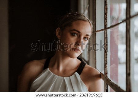 A beautiful woman gazing out a window with a somber look upon her face.  Royalty-Free Stock Photo #2361919613