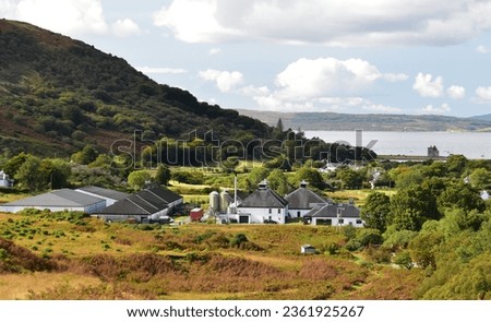 Lochranza Distillery, home of Arran Single Malt, nestled within the landscape on the Isle of Arran, Scotland with Lochranza Castle and the Kintyre peninsula in the distance on a bright autumn day. Royalty-Free Stock Photo #2361925267