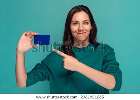Shot of beautiful woman holding a blue card while pointing at it with his finger on isolated on blue