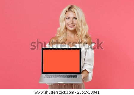 Smiling young blonde woman 20s wearing white casual clothes hold laptop pc computer with blank empty screen mock up copy space looking camera isolated on bright pink colour background studio portrait