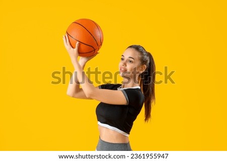 Sporty young woman with ball on yellow background