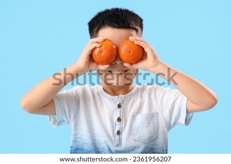 Little Asian boy with fresh tangerines on blue background