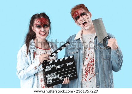Young couple dressed for Halloween as zombies with movie clapper on blue background