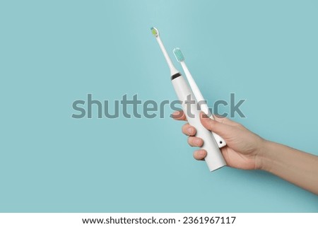 Woman holding electric and plastic toothbrushes on light blue background, closeup. Space for text