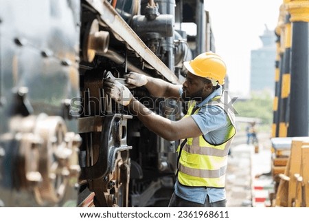 African American male engineer maintenance locomotive engine in locomotive repair garage. Male railway engineer use wrench repair train wheel in train garage Royalty-Free Stock Photo #2361968611