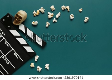 Composition with tasty popcorn, clapperboard and skull for Halloween celebration on green background