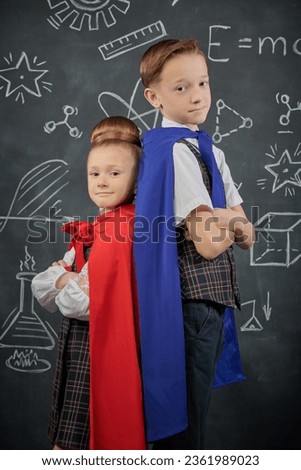 Cute little kids in cloaks make poses of superheroes. Education and early development. Little Scientists. Background of a black chalkboard.