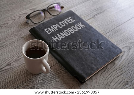 Closeup image of book with text EMPLOYEE HANDBOOK surrounded by cup of coffee and glasses on office desk Royalty-Free Stock Photo #2361993057