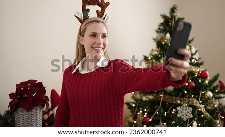 Young blonde woman make selfie by smartphone standing by christmas tree at home