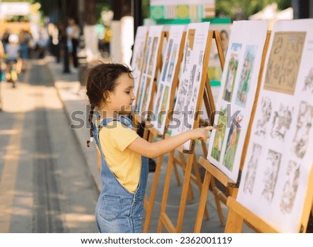 Little cute girl looks picture in street art gallery.