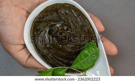 Hand holds Henna Paste with Leaves in Ceramic Bowl - top view