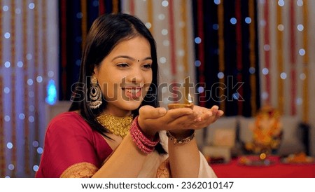Medium shot of a pretty Indian girl in traditional wear, showing a glowing oil lamp against a festive background. Bokeh shot - A beautiful young female holding a burning Diya on Diwali festival, of...