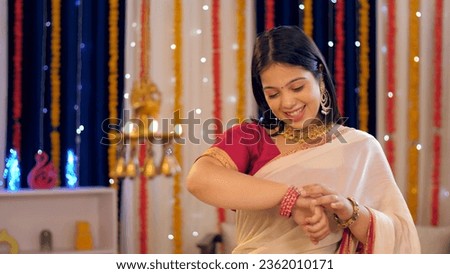 A beautiful Indian woman in an ethnic dress checking her new bangles - woman's accessories, festival celebration. A young woman wearing jewellery and a saree for Diwali festival - traditional dress... Royalty-Free Stock Photo #2362010171
